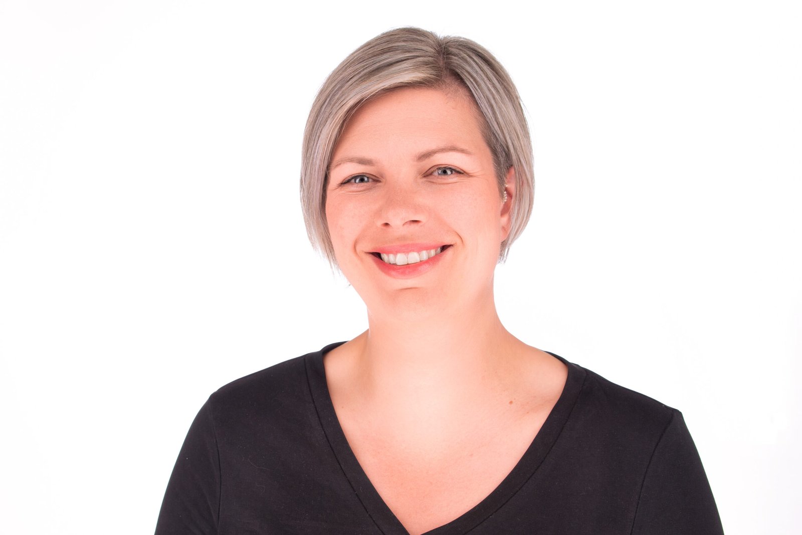 Smiling woman with short blonde hair wearing a black V-neck shirt against a white background.